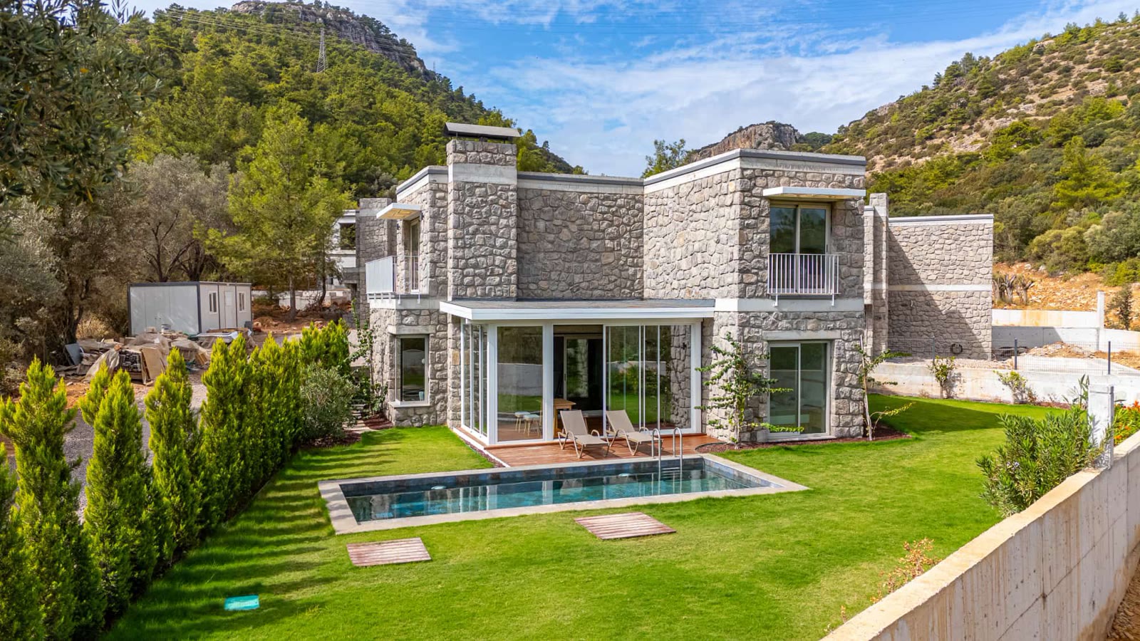 Rinnova Bodrum'da tamamlanmış taş örnek villa ve havuzu; arka planda şantiye konteyneri.