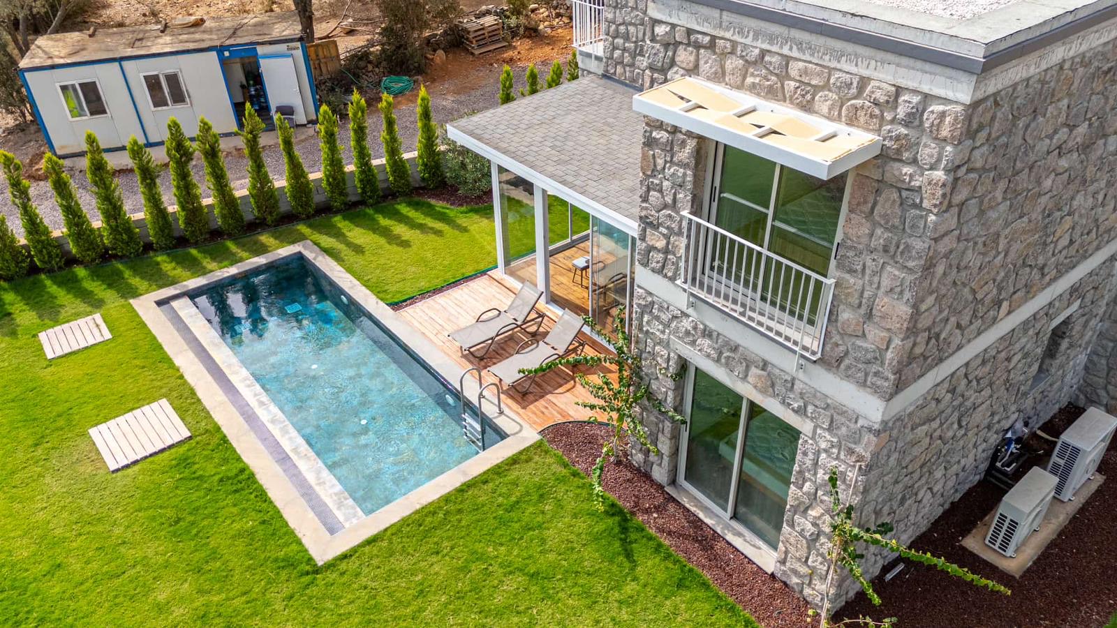 Aerial view of the Rinnova Bodrum show villa: swimming pool, timber deck and sun loungers, with a blue and white site cabin and building materials on the left.